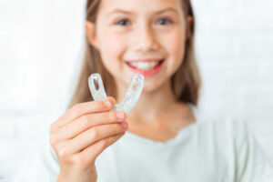 Niña sonriendo mientras sostiene una férula dental infantil, en Clínica Maranta, Santa Cruz de Tenerife.