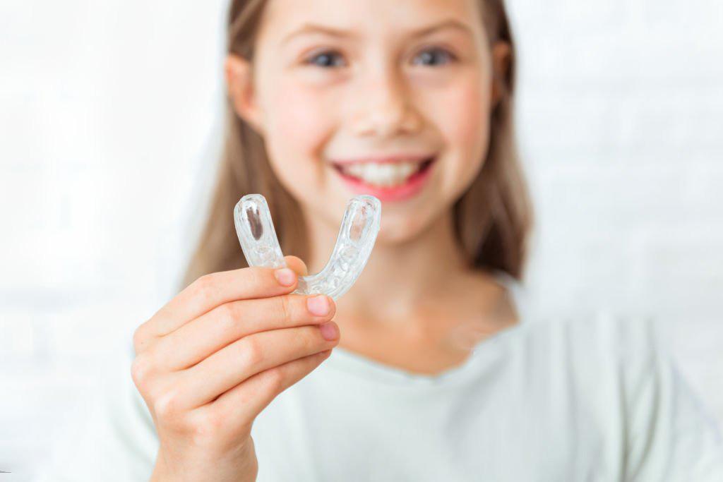 Niña sonriendo mientras sostiene una férula dental infantil, en Clínica Maranta, Santa Cruz de Tenerife.