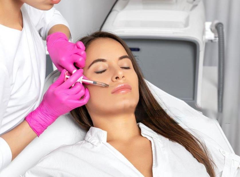 Aplicación de relleno facial en la zona de la mejilla por un profesional con guantes, mientras la paciente permanece relajada.